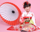 開いた番傘を背に座る着物姿の女児