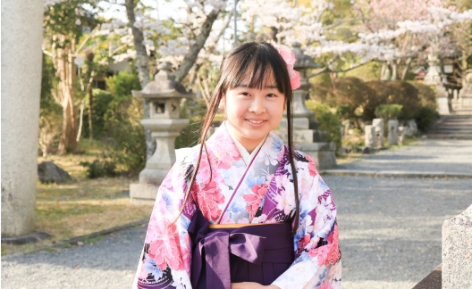 桜並木を背景に立つ青い着物と袴の女の子