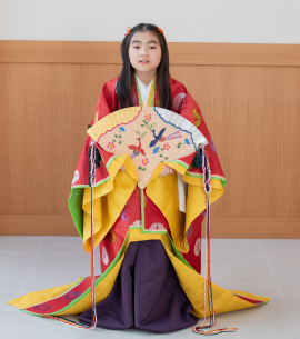 扇子を手に持つ、赤い十二単姿の7歳女児