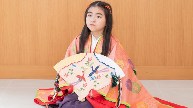 扇子を手に座る十二単姿の7歳の女の子