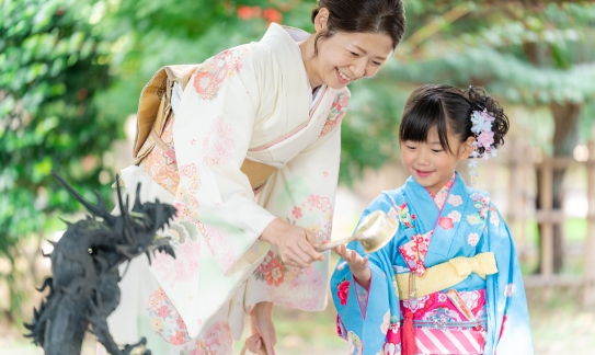 青い着物を着た少女に手水の柄杓を渡す母親